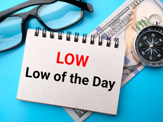Banknotes,compass and glasses with text LOW Low of the day on blue background.