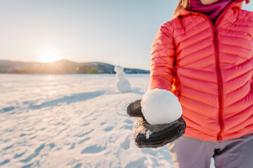 Winter outdoor active lifestyle concept. Girl holding snowball on snowy day with snowman in...