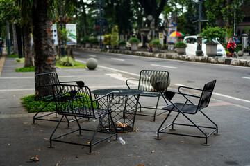 Empty public chairs in a park of Dago Street sidewalk during the pandemic, with a few trash strewn...
