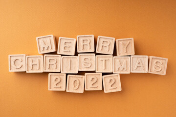 Merry Christmas 2022 is written on wooden cubes. Wooden cubes with letters and numbers on an orange background. New Year's card
