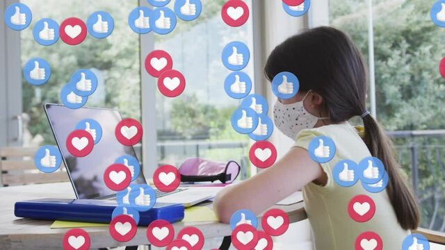 Animation of digital like and love icons over caucasian girl in face mask using laptop at home