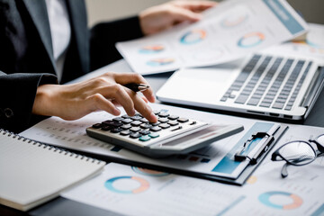 Close up of Businesswomen or Accountant using a calculator and laptop computer with analytic business report graph and finance chart at the workplace, financial and investment concept.