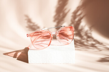 Fashionable pink sunglasses on geometric podium. Pampas grass natural shadows on beige background....