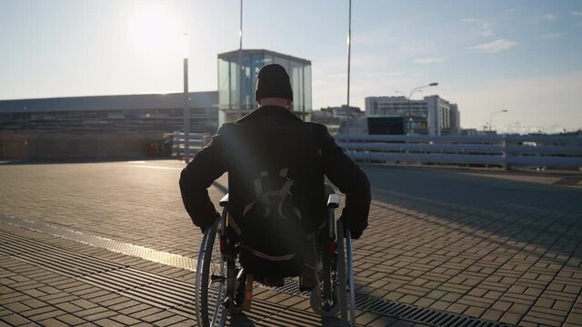 handicapped man in wheelchair in city, using manual invalid carriage for moving