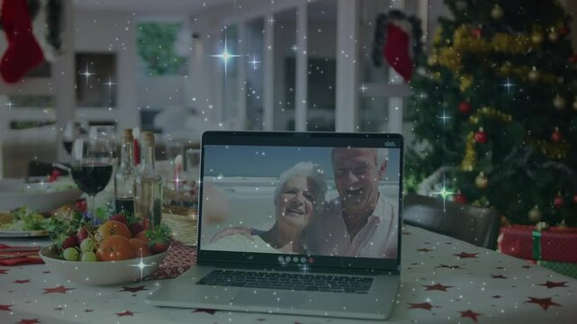 Animation of stars over christmas table and senior couple on laptop screen making video call