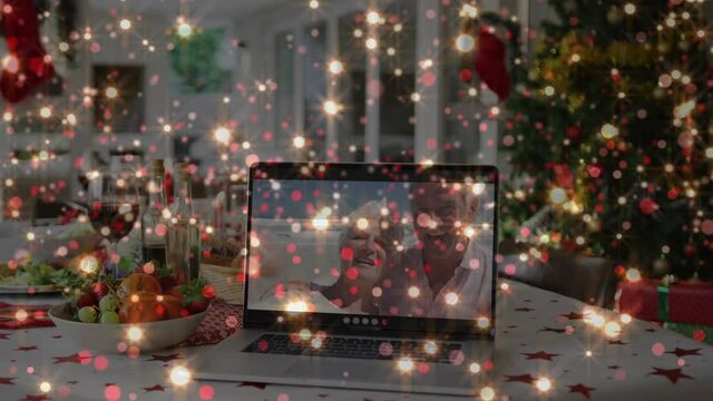 Animation of glowing lights over christmas table and happy senior couple on laptop video call