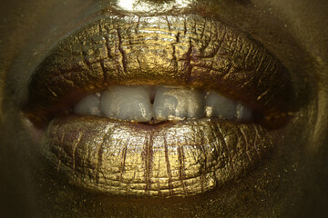 Obraz premium Golden lips macro close up. Gold lips. Gold paint from the mouth. Golden lips on woman mouth with make-up. Sensual and creative design for golden metallic.