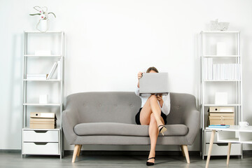 Young attractive sexy secretary in office. Beautiful secretary legs. Seductive sexy secretary freelancer with laptop computer and sexy legs sit on sofa in office. Sensual young girl employee.