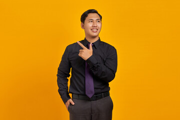 Cheerful young handsome businessman pointing finger away at copy space on yellow background
