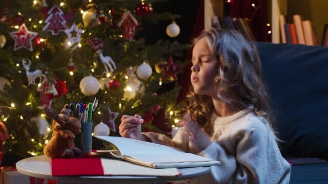 Little girl drawing toy, sitting on sofa in decorated living room. Small child painting deer, using colorful markers. Hobby and leisure during christmas holidays. New year atmosphere, happy childhood.