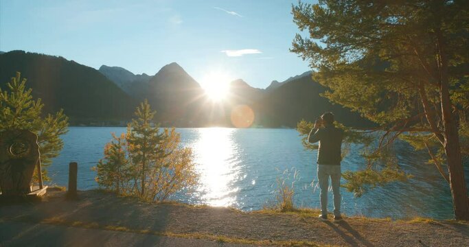 Male tourist recording scenic view of alps mountains at lake achensee in sunset golden hour in Austria, Europe. Wide Angle.
