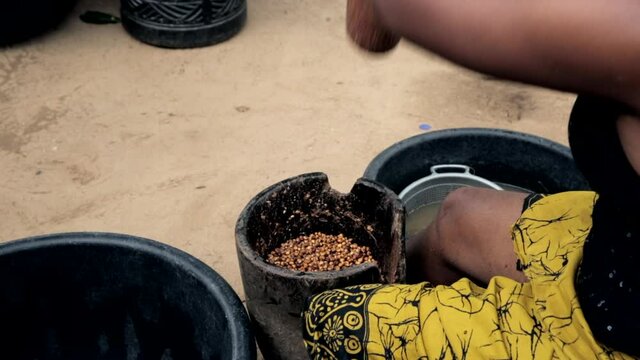 Woman in rural Nigeria, West Africa pounding tiger nut into flour in a motor and pestle - over shoulder view