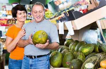 Fototapeta premium Adult happy male and female are choosing green melons in the store.