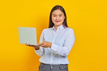 Photo of cheerful young business woman with confident face using laptop and looking at camera isolated over yellow background