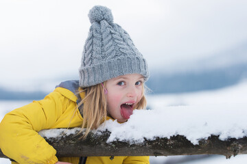 Winter girl eating snow outdoor. Funny christmas kids holiday. Kids cold and flu concept. Kid lick snow with tongue. Children wearing warm winter clothing in snow weather. Funny kids face. - obrazy, fototapety, plakaty