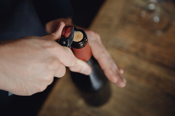 Sommelier opens cork of bottle of red wine with corkscrew, top view