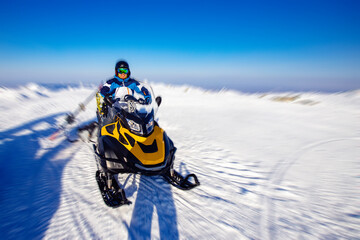 Happy snowmobile driver on blue sky background, motion blur effect