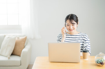 家でテレワークする女性（スマホで電話）
