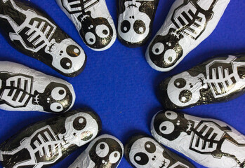 Trick or treat chocolate candies in the shape of black and white skeletons on blue background with round frame for text inside it. Halloween sweets and treats. October 31st. Funny scary characters