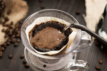 The teapot is pouring hot water over the ground coffee beans into the cup passing the drip coffee filter bag onto the cup