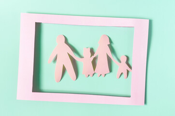 Cardboard figures of adults and children on a blue background in a pink frame. The concept of family relations.