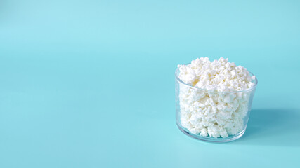Fresh cottage cheese made from milk in a transparent dish on a blue background. White cottage cheese in a bowl on a light background copy space