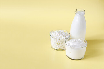 Sour cream and cottage cheese in a glass container on the background of a bottle of milk yellow background