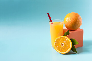 Orange juice in a transparent glass with a decor of oranges and green leaves on a blue background advertising