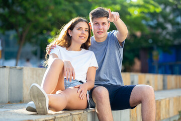 Young man prompts the girl, pointing with his hand at something
