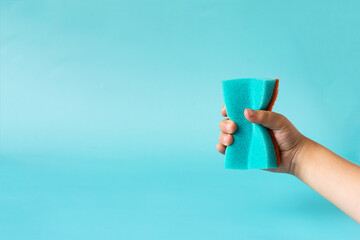 Action The hand holds a blue sponge on a colored background. The concept of washing dishes and...