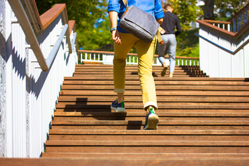 Businessman freelancer, student. Man guy in casual style runs up wooden steps of staircase in hurry to run errands. Big city resident with large crossbody bag, portfolio running up. People on a street