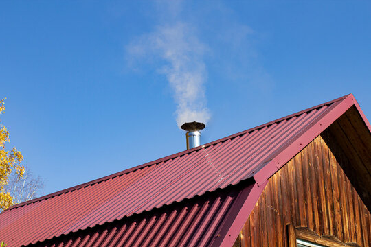 Steel roof of a private house with chimney and smoke against the backdrop of a beautiful blue sky.
