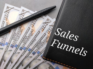 Banknotes,pen and notebook with text Sales Funnels on a gray background.