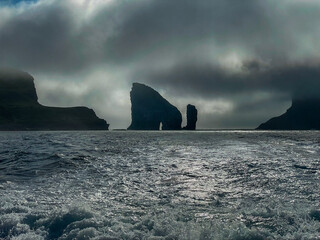 View of the impressive Rocky Drangarnir sea stack and the fishing farms in the Faroe Islands seen from the ferry to Mykines 