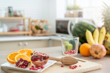 Freshly cut juicy orange slices and pomegranate on white plate at kitchen, fruits on blurred background, selective focus