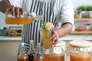 Man in apron pouring kombucha from bottle to made Kombucha cocktail, lemon and rosemary, lemon...