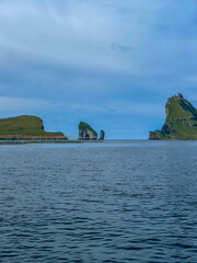 Fototapeta premium View of the impressive Rocky Drangarnir sea stack and the fishing farms in the Faroe Islands seen from the ferry to Mykines 