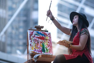 Female street artist in a hat paints a picture on the city