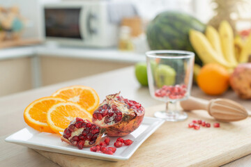 Freshly cut juicy orange slices and pomegranate on white plate at kitchen, fruits on blurred background, selective focus