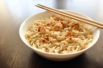 Instant noodles with dry red chilli flakes and seasoning on a white plate. 