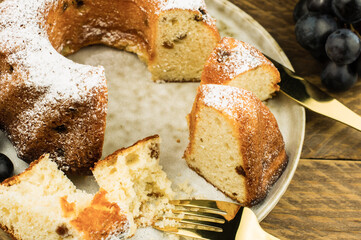 foreground of a sliced cupcake with raisins and powdered sugar on a plate and a wooden background.