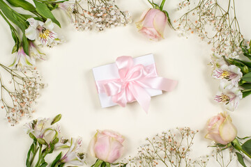 A white gift box with a pink bow on a pink background in a frame of fresh flowers. A gift for a holiday. Congratulation. A greeting card. Sale. Black Friday. Happy Birthday
