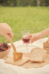 picnic concept someone handing a glass of grapes juice to another who tries to pick up a crispy bread while being on a picnic