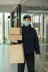 Parcel delivery concept the standing-tall post carrier who is wearing pale grey cap carrying one bag on left hand and two boxes on right hand and being ready to drop these stuffs to his customers