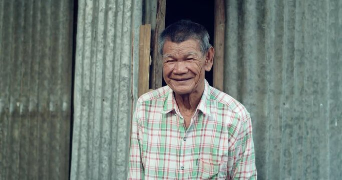 An Asian man who is more than seventy years old and works as a wage earner in a farm, live in a poor house, smiling and laughing happily  in a countryside.