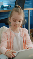 Young child using keyboard on laptop for homework and online courses for distance education. Little girl looking at screen and working for school task and remote learning at home.