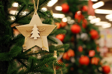 Christmas tree with wooden toy in star shape on a branch. New Year decorations on blurred lights...
