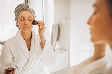 Young woman applying face cream by the mirror