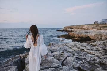 Woman in white dress rocks ocean walk back view