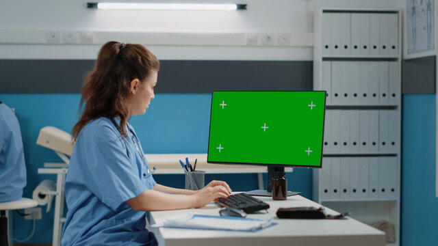 Healthcare assistant using computer for horizontal green screen in cabinet. Medical nurse working with chroma key on monitor for isolated background and mockup template. Woman with gadget
